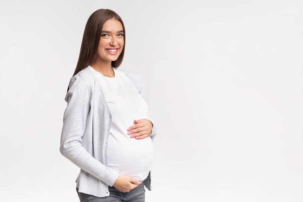 Joyful Expectant Woman Touching Belly Posing Over White Studio Background - Foto, afbeelding