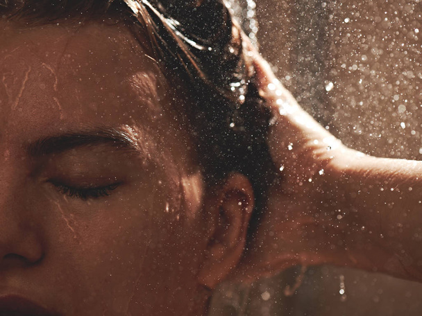 Duştaki kız saçlarını suyla yıkıyor, yüzünü ıslatıyor, gözlerini kapatmaktan hoşlanıyor. - Fotoğraf, Görsel