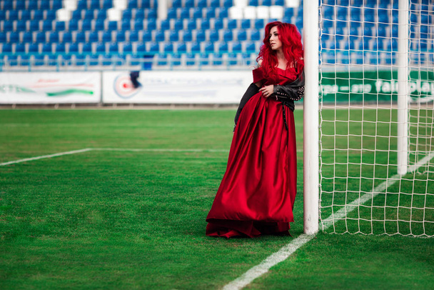 Luxusní žena s rudými vlasy a v červených šatech hraje na fo - Fotografie, Obrázek