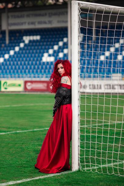 Luxurious woman with red hair and in a red dress plays on the fo - Photo, Image