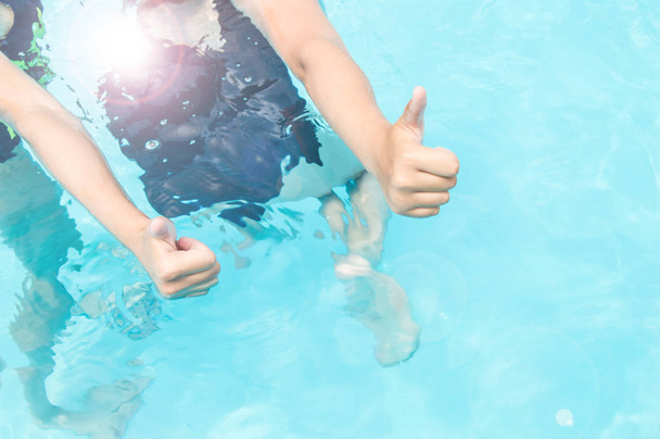 Daumen hoch zwei Teenager-Mädchen mit langen Haaren in Badeanzügen in einem Pool mit blau glitzerndem Wasser im Freien, Sonnenlicht, gleißendem Sommer - Foto, Bild