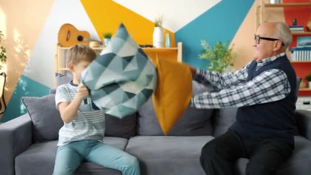 Playful people old man and cute boy enjoying pillow fight having fun at home - Filmagem, Vídeo