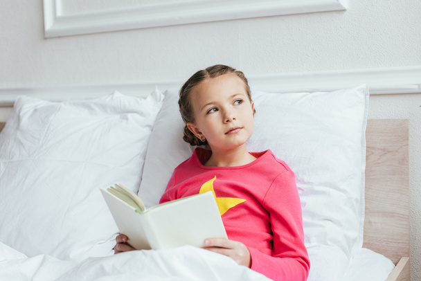 duur kind lezen boek terwijl zitten op bed - Foto, afbeelding