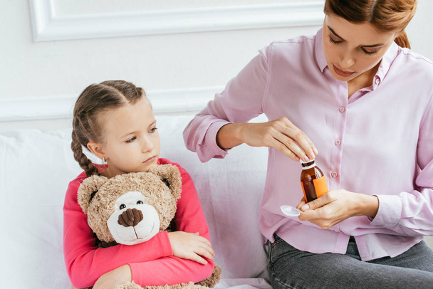 moeder geven siroop naar ziek dochter met teddy beer - Foto, afbeelding