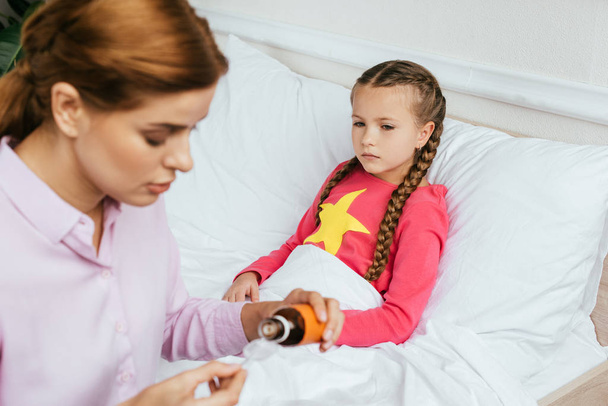 worried mother giving syrup to sick daughter in bed - Photo, Image
