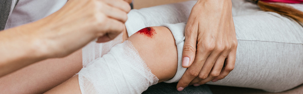 panoramic shot of mom wounding bandage around knee of daughter - Foto, afbeelding