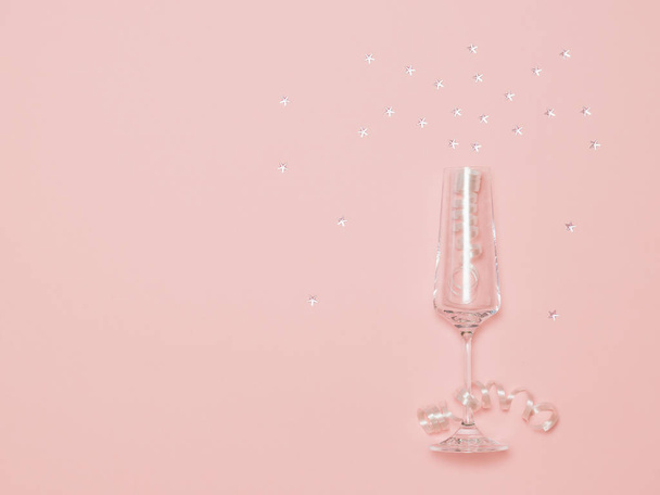 elegantes Champagnerglas mit Serpentinen und leuchtenden Pailletten auf rosa Hintergrund. - Foto, Bild