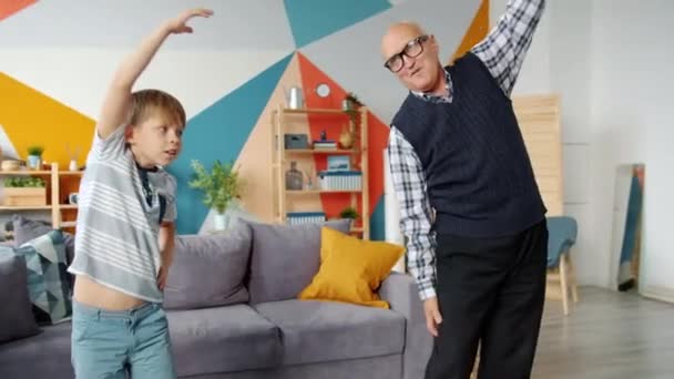 Abuelo jubilado y lindo niño hacen ejercicios físicos juntos en casa
 - Imágenes, Vídeo