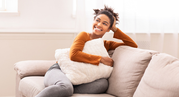 African American Woman Sitting On Sofa Embracing Pillow Indoor, Panorama - Photo, Image
