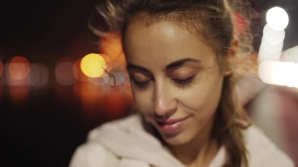 Close-up slowmotion van mooie glimlachende jonge vrouw wandelen buiten nacht stad. - Video