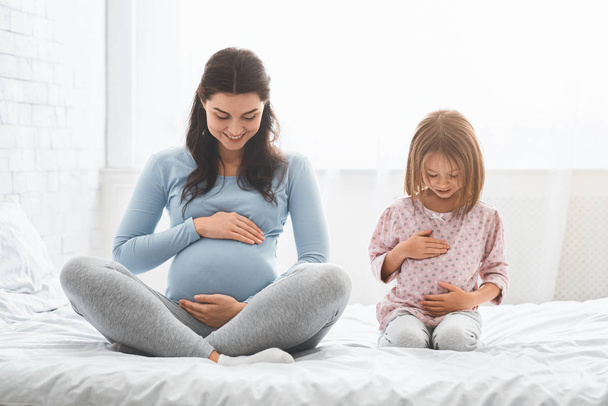 Filhinha imitando sua mãe grávida, tocando sua barriga
 - Foto, Imagem