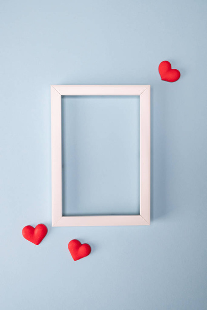 Minimal valentine day concept. White empty photo frame with hearts on blue background. Flat lay, top view, copy space . Template for greeting card, seasonal promotions and discounts - Foto, imagen