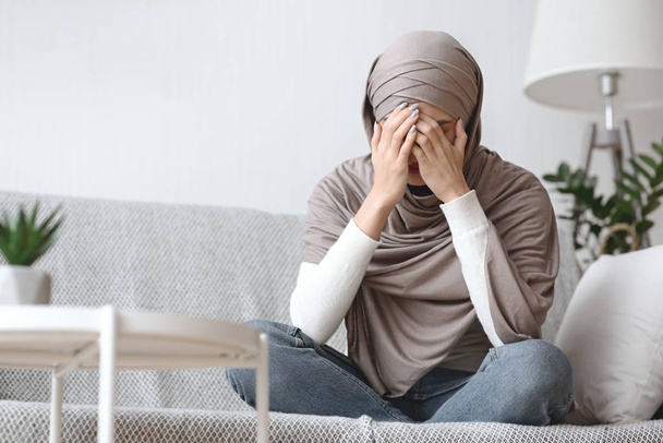 Chorando mulher muçulmana no hijab sentado no sofá em casa
 - Foto, Imagem