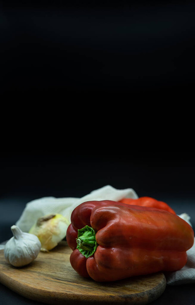 Red pepper, onions, garlic and zucchini in string bag on a wooden board, black background, zero waste concept - Фото, зображення