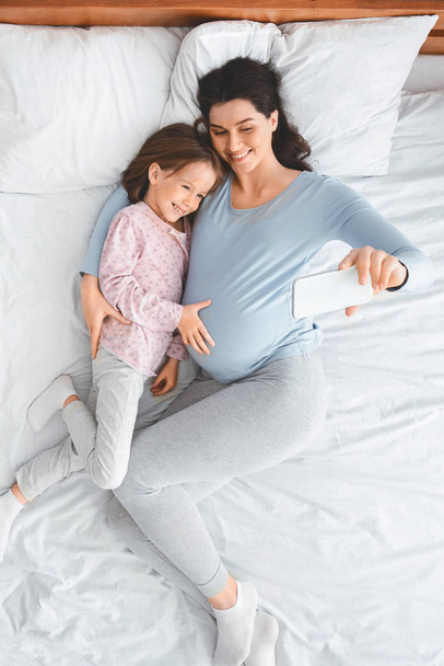 Ожидая, что мать и дочь будут лежать на кровати, делать селфи
 - Фото, изображение