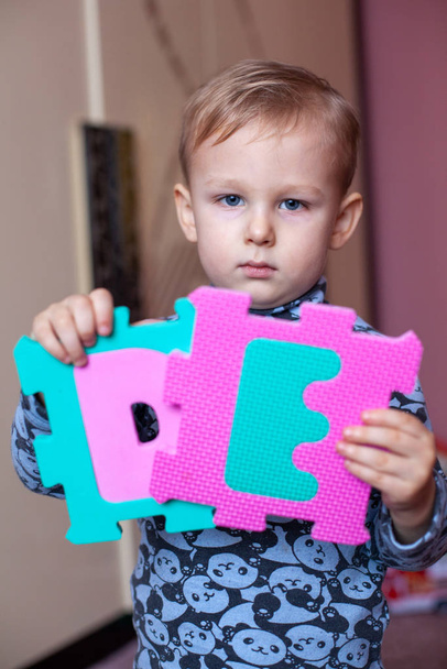 Little boy collects the puzzle sitting on floor. Big ABC squishy foam puzzle. Learning alphabet with puzzle mat - Photo, Image
