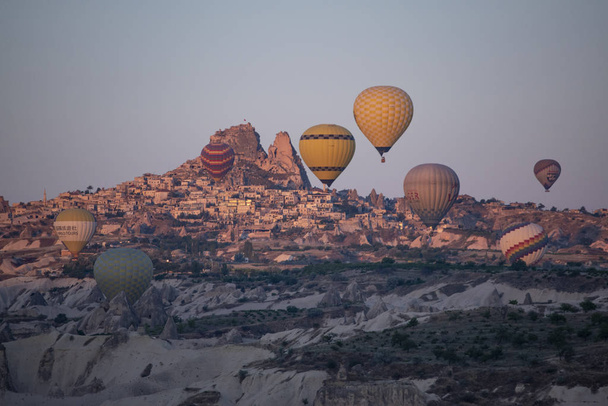 Cappadocia, Turkey, Europe, 07/08/2019: aerial view of Uchisar, ancient and famous town of the historical region in Central Anatolia rich of exceptional natural wonders, with hot air balloons floating in a breathtaking pink sky at dawn - Foto, imagen