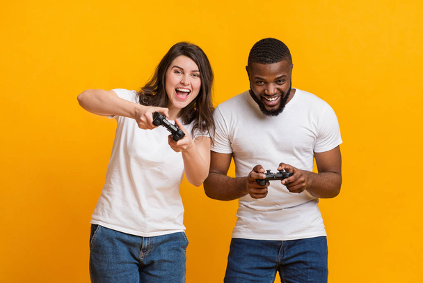 Iloinen rotujenvälinen pari tilalla joysticks kilpailevat keskenään videopelejä
 - Valokuva, kuva