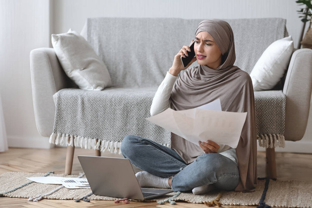 Huolestunut nainen työskentelee papereiden kanssa ja puhuu kännykkään kotona
 - Valokuva, kuva