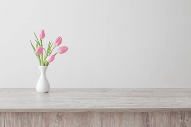 pink tulips in white ceramic vase on wooden table on background  - 写真・画像