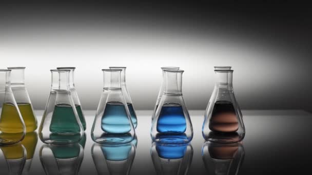 Empty and mixed color liquid filled erlenmeyer flasks reflecting on table - Footage, Video