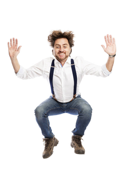 A smiling pretty redhead man with a beard in jeans and a white shirt is jumping. Isolated over white background.  - Φωτογραφία, εικόνα