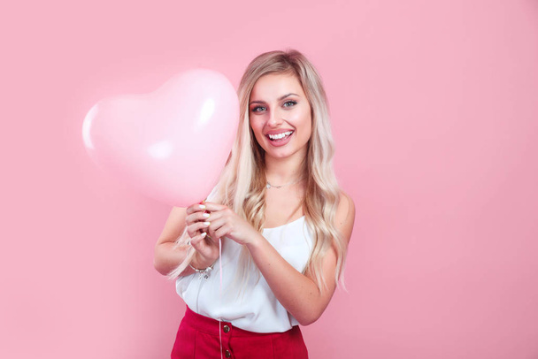 Mooie jonge vrouw met roze hart vorm luchtballon op kleur achtergrond. Vrouw op Valentijnsdag. - Foto, afbeelding