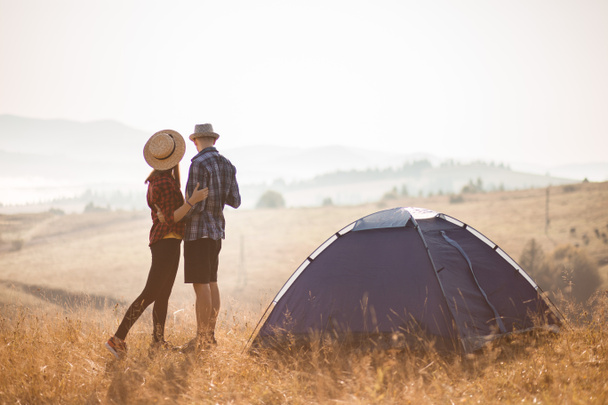 幸せな観光客のカップルはテントの近くの山の上を歩き、休暇中の秋の朝を楽しむ. - 写真・画像