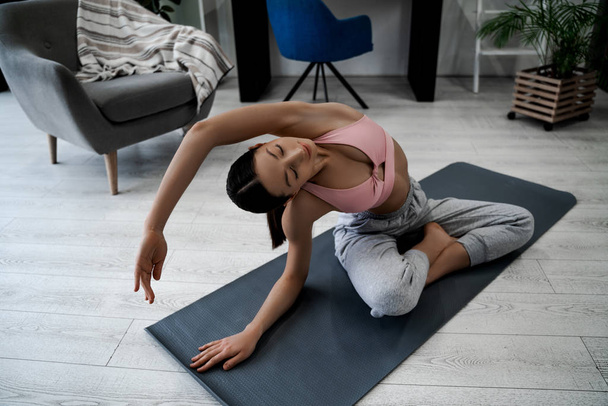 Jonge vrouw thuis doet yoga asana zelf, gelukkig gezicht en gezonde levensstijl, gezonde sterke atletische lichaam. Thuisbeweging in de ochtend voor het werk. Yoga, sport, levensstijl - Foto, afbeelding