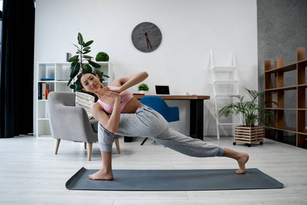 Sporty strong woman fitness trainer in sports yoga shows asana pose, playing sports without leaving home in the living room, morning exercises, healthy lifestyle, strong healthy body - 写真・画像