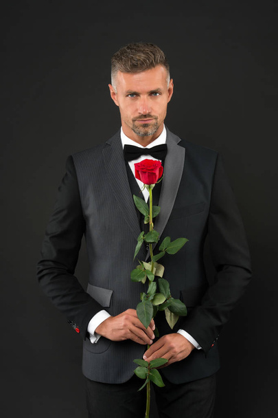 man dressed up in tuxedo with rose. Groom with tie and red rose. her elegant valentine. man tuxedo hold rose. man in tuxedo offers marriage. tailcoat or frac. red rose symbol of love. romantic love - Foto, immagini