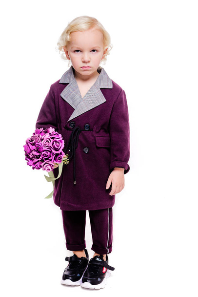 Petit garçon à la mode dans un élégant costume bordeaux et avec un bouquet de fleurs à la main sur un fond blanc. Le garçon est triste, contrarié, en colère
 - Photo, image