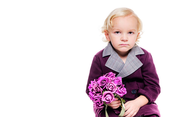 Petit garçon à la mode dans un élégant costume bordeaux et avec un bouquet de fleurs à la main sur un fond blanc. Le garçon est triste, contrarié, en colère
 - Photo, image