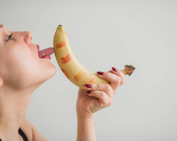Close-up of the face, lips, tongue of a young, European girl licking a big yellow, sweet banana. - Foto, Imagem