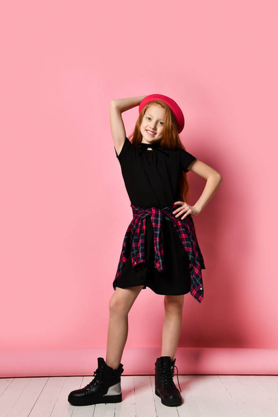 Ginger teenage girl in black dress, checkered shirt on waist, red hat and choker. She smiling, posing on pink background. Close up - Foto, Imagem