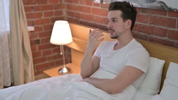 Rozrušený mladý muž sedí a stává se starosti v posteli - Záběry, video