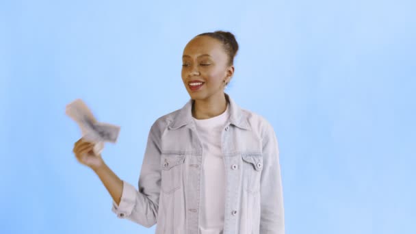 Satisfied african american woman with money is showing thumb up on blue background Jean jacket - Séquence, vidéo