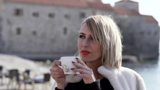 Beautiful girl drinks morning coffee on the beach - Filmati, video