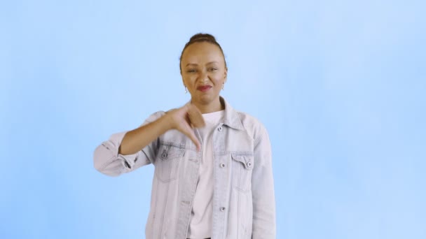 Genç mutsuz Afrikalı Amerikalı kadın mavi arka plan kot ceketini reddediyor. - Video, Çekim