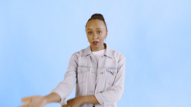 Portret van een overstuur Afrikaans Amerikaans meisje dat verbijsterd in de camera kijkt op een blauwe achtergrond. Gezicht palm expressie Jean jas - Video