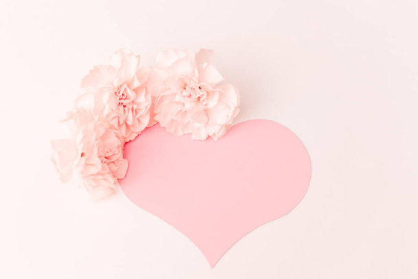 Un gran corazón rosa con un lugar para el texto decorado con tres pequeñas flores de clavo rosa sobre un fondo blanco
 - Foto, imagen