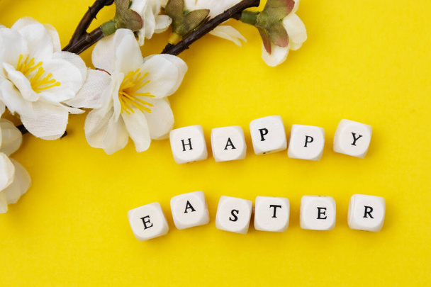 Happy Easter. Cubes with text on yellow background. Spring brunches with white flowers. Minimalistic flat lay. - Foto, Imagen
