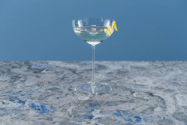clear alcohol drink in wineglass with lemon peel decoration - Photo, Image