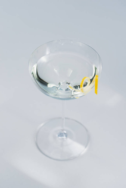 clear alcohol drink in wineglass with lemon peel decoration - Photo, image