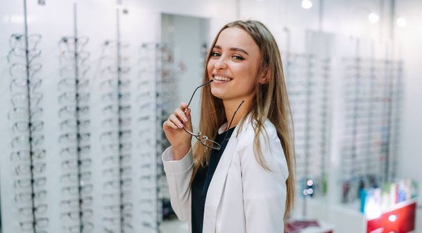 Beautiful young woman choosing new pair of spectacles in opticians store. Eyesight correction. Optics. Ophthalmology. - Photo, image