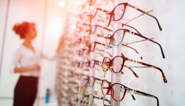 Row of glasses at an opticians. Eyeglasses shop. Stand with glasses in the store of optics. Woman chooses spectacles. Eyesight correction. - Photo, image