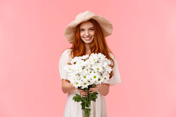 C'est pour toi, félicitations. séduisante belle jeune fille rousse charismatique donnant bouquet de fleurs blanches et souriant, félicitations avec anniversaire, exprimer l'amour et les soins, debout fond rose - Photo, image