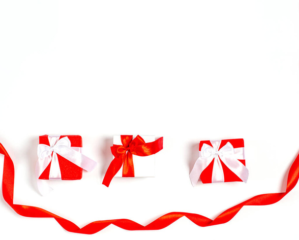 Concetto di San Valentino. Scatole regalo con nastri rossi e un ampio nastro rosso in basso su sfondo bianco
. - Foto, immagini