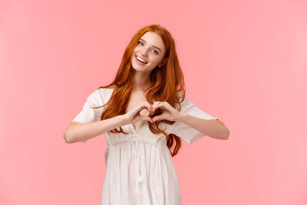 Waist-up portrait lovely, romantic and cute european woman with red hair, tilt head and smiling, saying love you, make heart gesture in like, express affection or sympathy, happy valentines day - Fotoğraf, Görsel