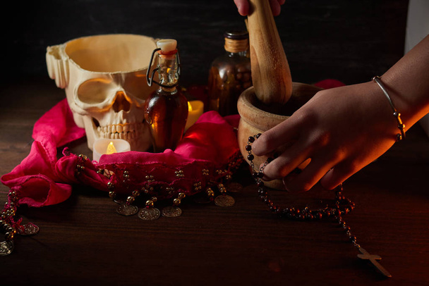 Hand using mortar Scary still life with potions, skull, mortar, vintage bottles and candles on witch table. Halloween or esoteric concept. - Photo, Image